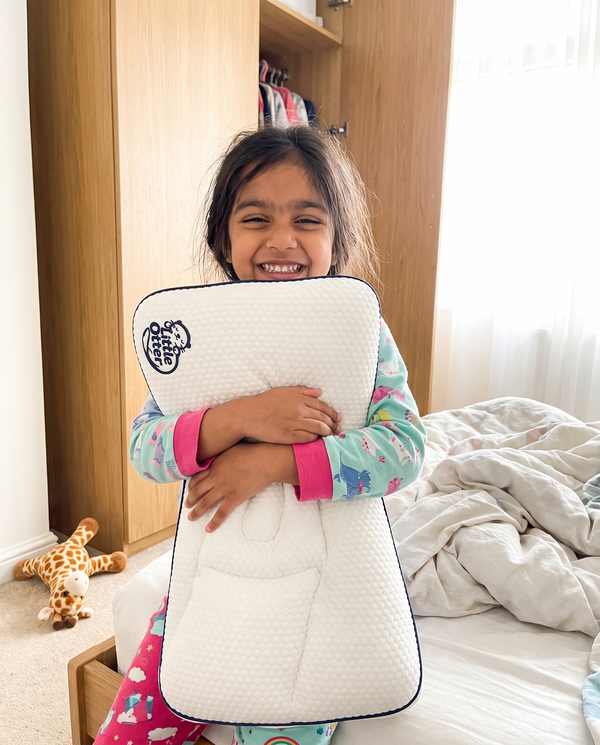 A girl sitting up in bed hugging her Little Otter pillow in the morning